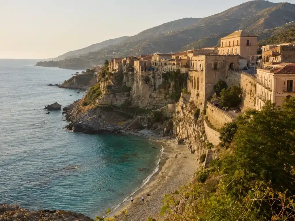 Calabrian coastal town on a Tyrrhenian cliff above turquoise water at golden hour with Aspromonte hills behind