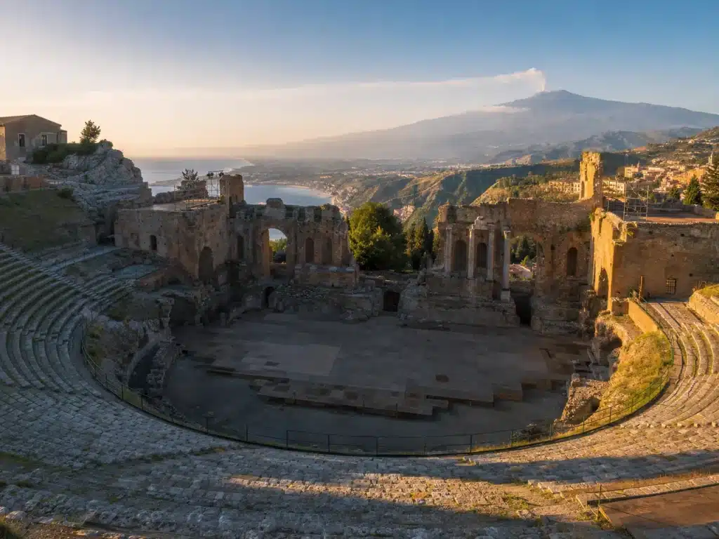 The Greek Theatre of Taormina at sunrise, its stone tiers framing the Ionian Sea and Mount Etna